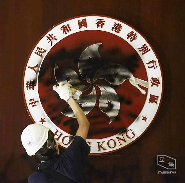 A pro-democrocy protester sprays black spray-paint on the emblem of the Hong Kong Special Administrative Region inside the Legislative Council Chamber on July 1, 2019. Photo Credit: The Stand News. 